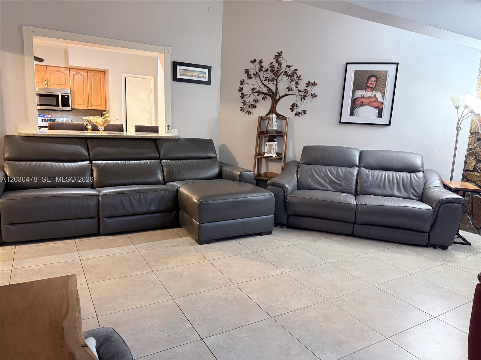 A living room features gray leather sofas, tile flooring, and a view into the kitchen — 18240 NE 8th Ave, North Miami Beach FL 33162, NORTH MIAMI BEACH, FL