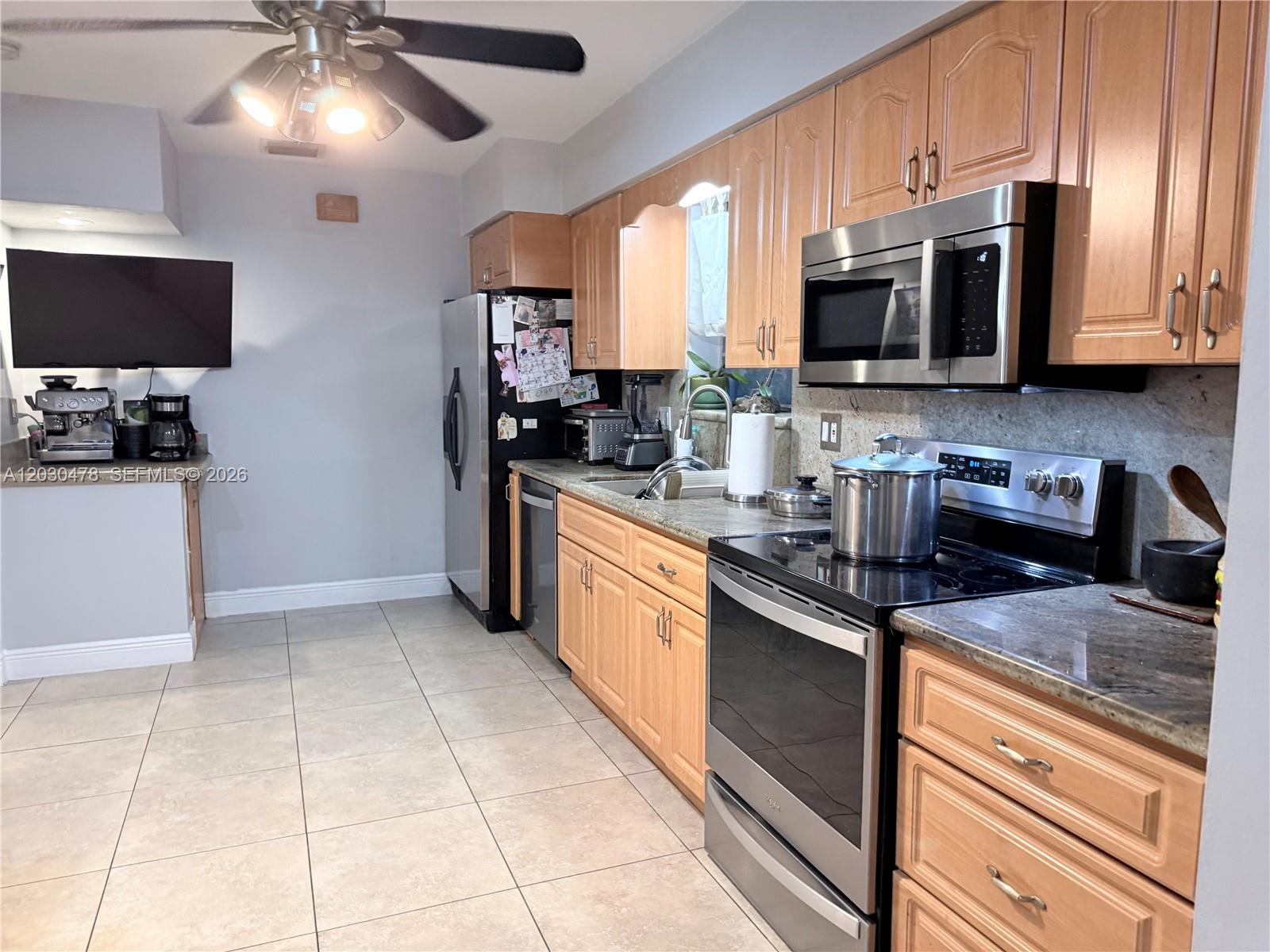 A kitchen features light wood cabinets, stainless steel appliances, and beige tile flooring — 18240 NE 8th Ave, North Miami Beach FL 33162, NORTH MIAMI BEACH, FL