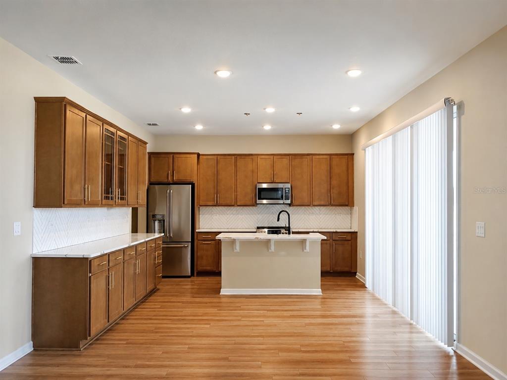 A kitchen features wood cabinets, stainless steel appliances, a center island, and light-colored countertops — 1028 SUGARWOOD STREET, DAVENPORT, FL