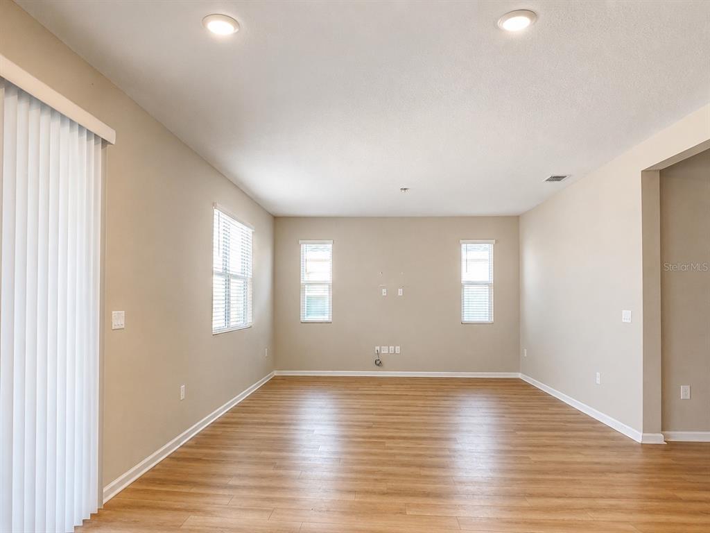 An empty living room features light-colored walls, wood-look flooring, recessed lighting, and several windows — 1028 SUGARWOOD STREET, DAVENPORT, FL