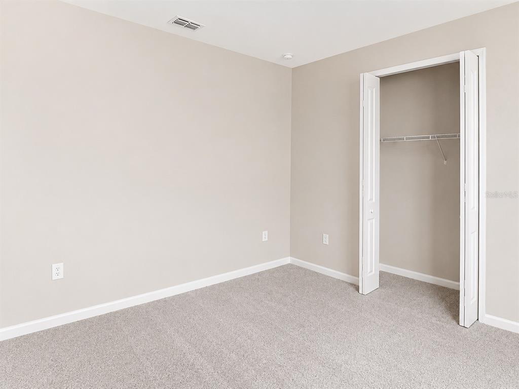 An empty bedroom with beige walls, gray carpeting, and an open white closet — 1028 SUGARWOOD STREET, DAVENPORT, FL