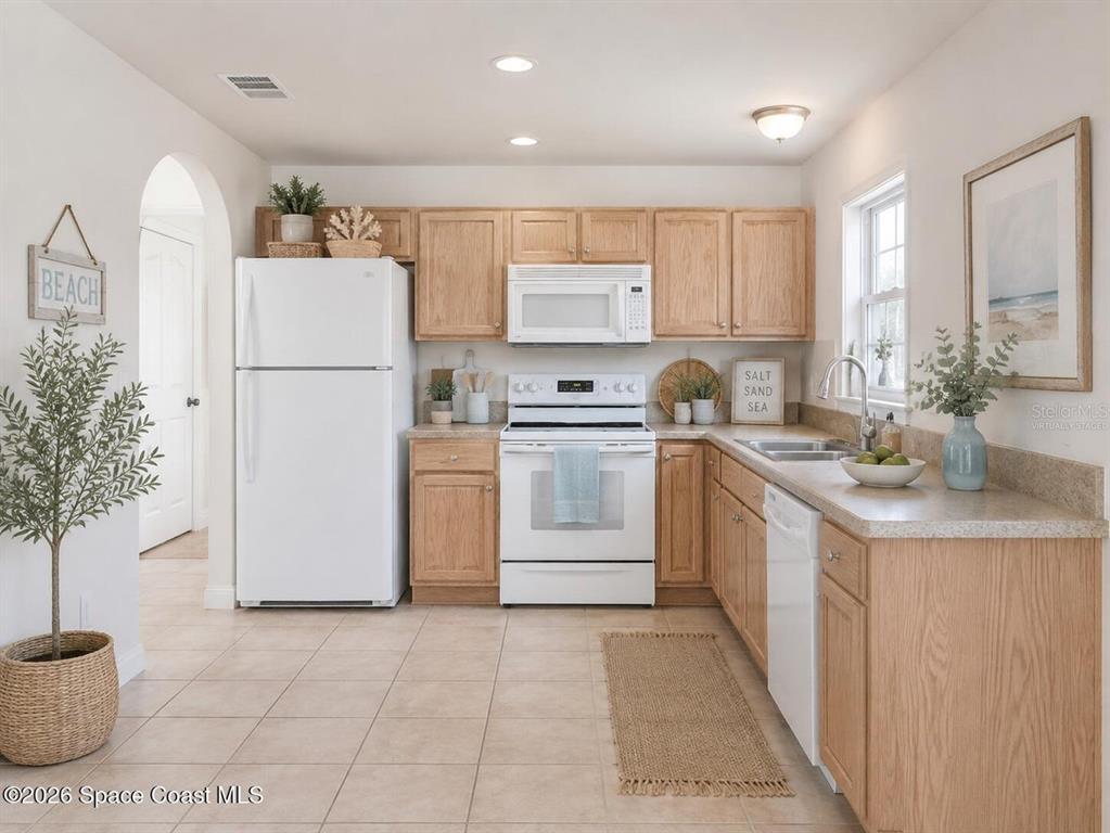 A kitchen features light wood cabinets, white appliances, tile flooring, and a beige countertop — 1582 PENTAX AVENUE, TITUSVILLE, FL