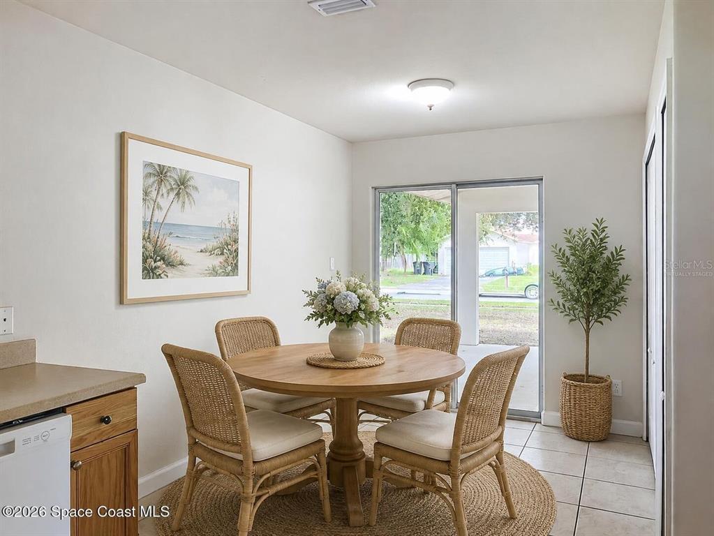 A dining area features a round wooden table with four wicker chairs and sliding glass doors — 1582 PENTAX AVENUE, TITUSVILLE, FL