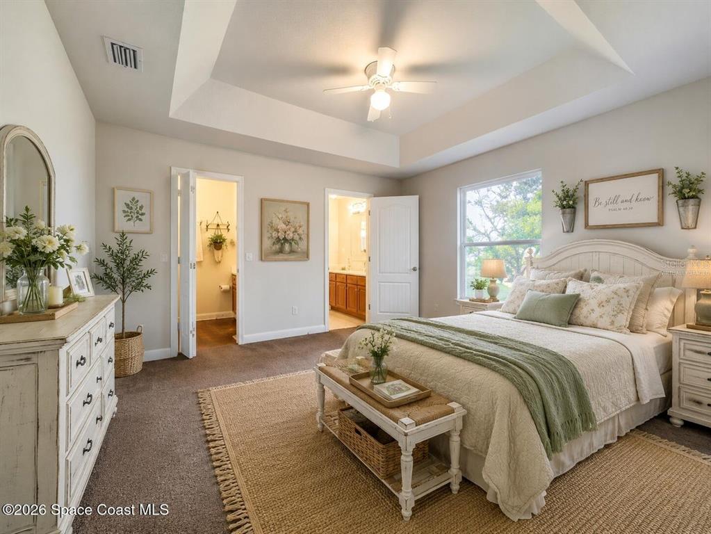 A bedroom with a tray ceiling, carpeted floors, a queen bed, and an attached bathroom — 1582 PENTAX AVENUE, TITUSVILLE, FL