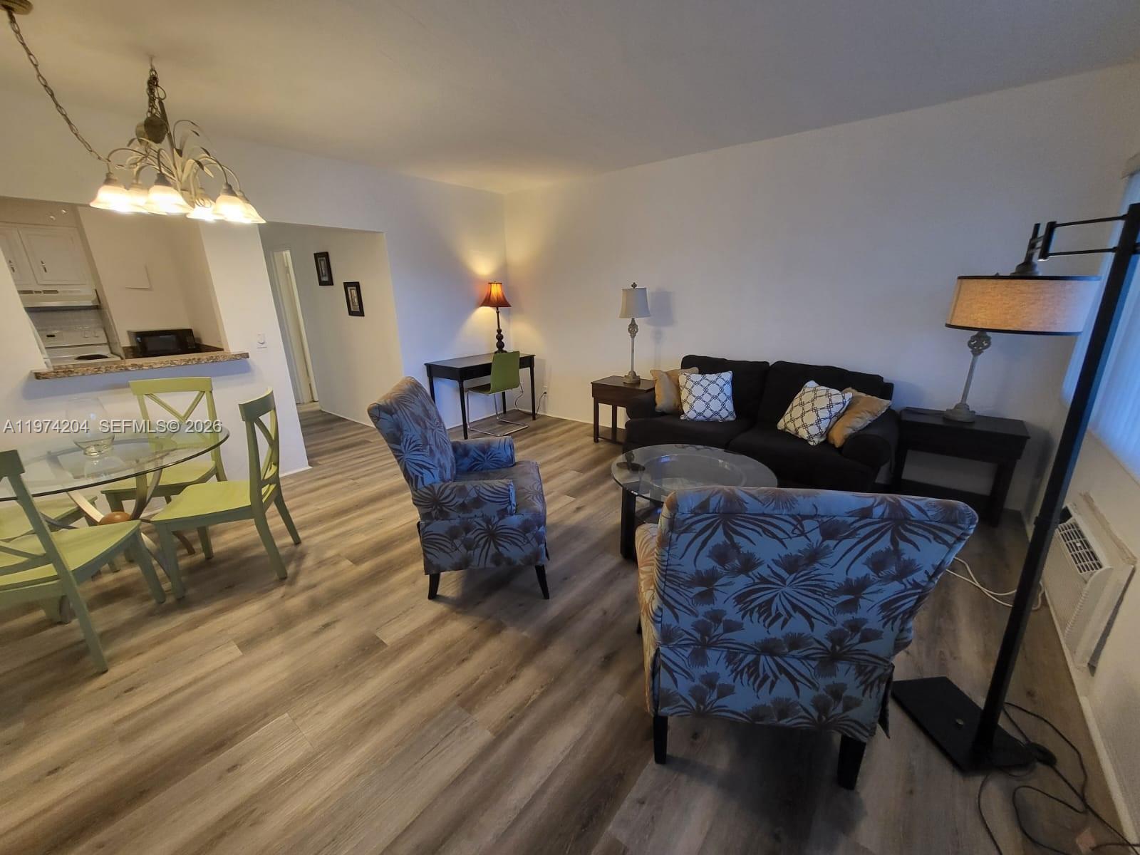 A living and dining area features wood-look flooring, a dark sofa, and two patterned armchairs — 600 Layne Blvd # 216, Hallandale Beach FL 33009, HALLANDALE BEACH, FL