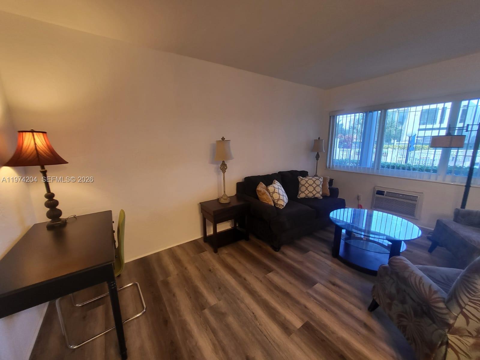 A living room features wood-look flooring, a dark sofa, a glass coffee table, and a desk — 600 Layne Blvd # 216, Hallandale Beach FL 33009, HALLANDALE BEACH, FL