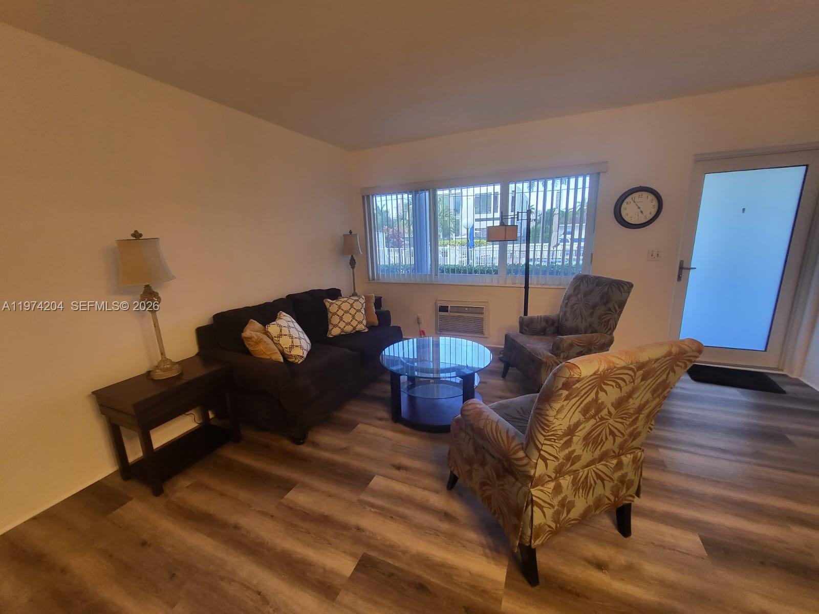 A living room features a dark sofa, two patterned armchairs, and wood-look flooring — 600 Layne Blvd # 216, Hallandale Beach FL 33009, HALLANDALE BEACH, FL