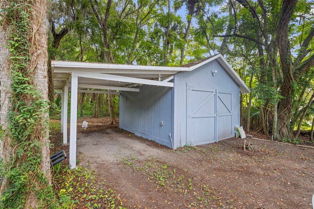 A light blue detached garage with an attached carport sits in a wooded yard — 135 S ARLINGTON AVENUE, DELAND, FL
