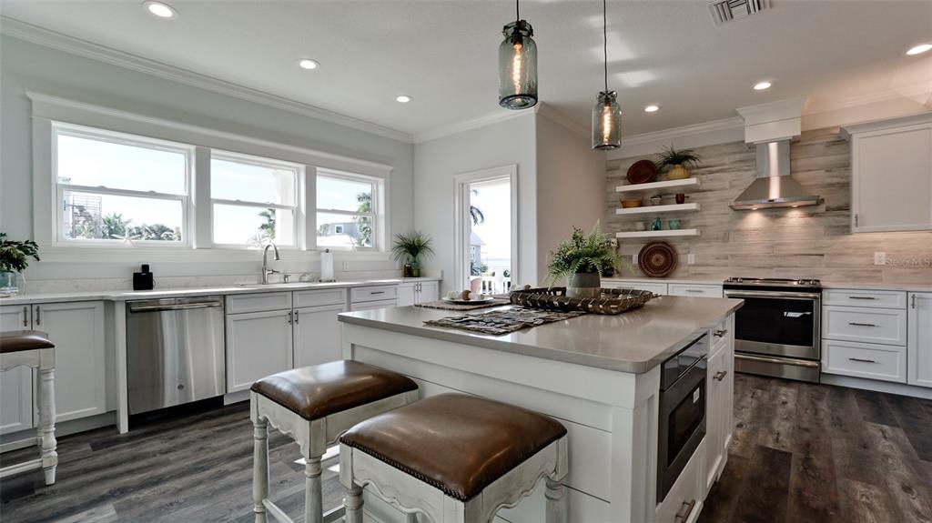 A kitchen features white cabinets, a central island with bar stools, and wood-look flooring — 8202 17TH AVENUE W, BRADENTON, FL
