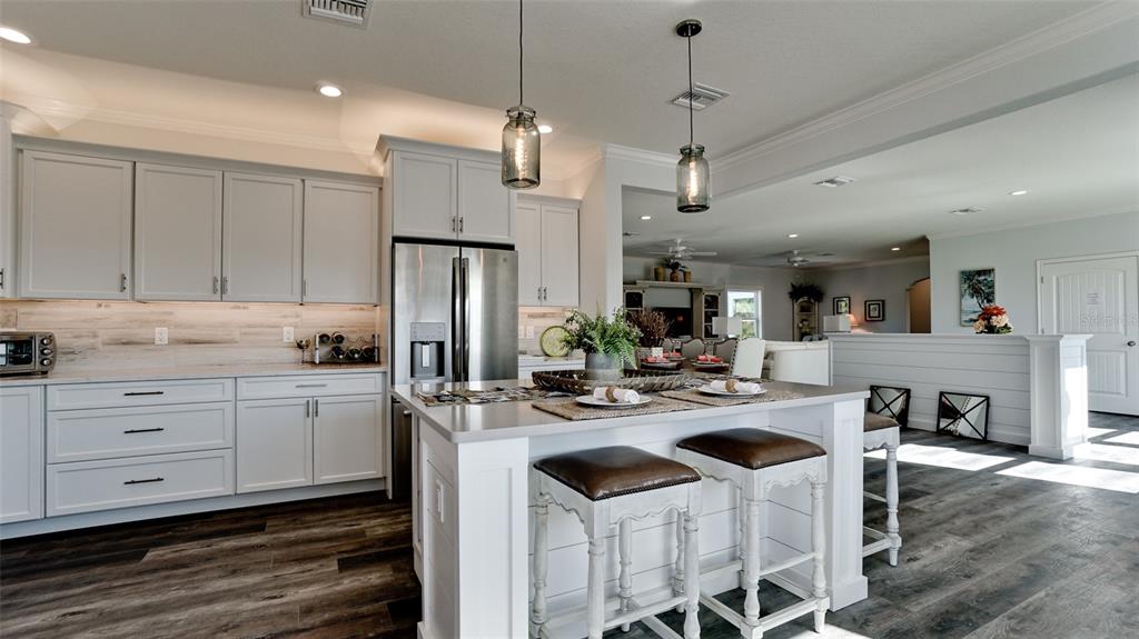A kitchen features white cabinetry, a central island with bar stools, and dark wood flooring — 8202 17TH AVENUE W, BRADENTON, FL