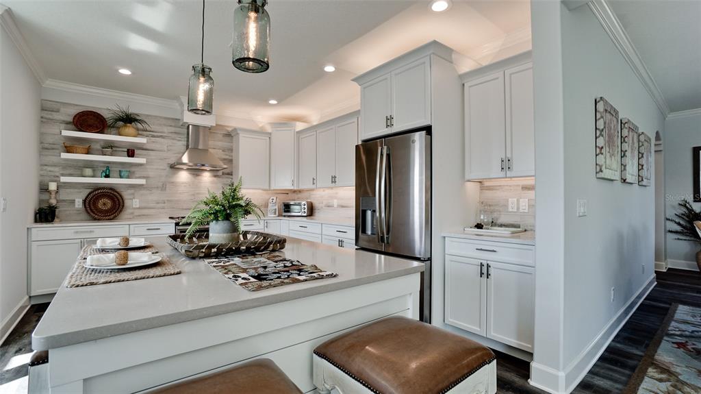 A modern kitchen features white cabinetry, a large gray island, and a wood-plank accent wall — 8202 17TH AVENUE W, BRADENTON, FL