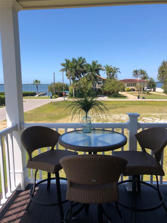 A covered porch features a small bistro table and three wicker chairs overlooking a waterfront view — 8202 17TH AVENUE W, BRADENTON, FL
