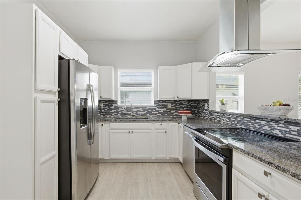 A kitchen with white cabinets, stainless steel appliances, granite countertops, and a gray tile backsplash — 2815 N TALIAFERRO AVENUE, TAMPA, FL