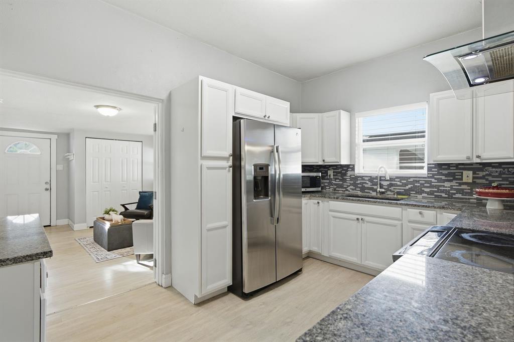A kitchen with white cabinets, stainless steel appliances, and granite countertops leads into a living area — 2815 N TALIAFERRO AVENUE, TAMPA, FL