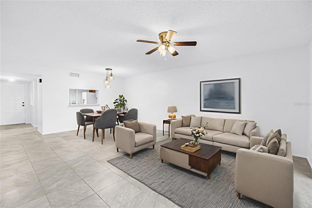 An open-concept living and dining area features white walls, tile flooring, and neutral furniture — 3600 MAGNOLIA RIDGE CIRCLE UNIT 1224, PALM HARBOR, FL