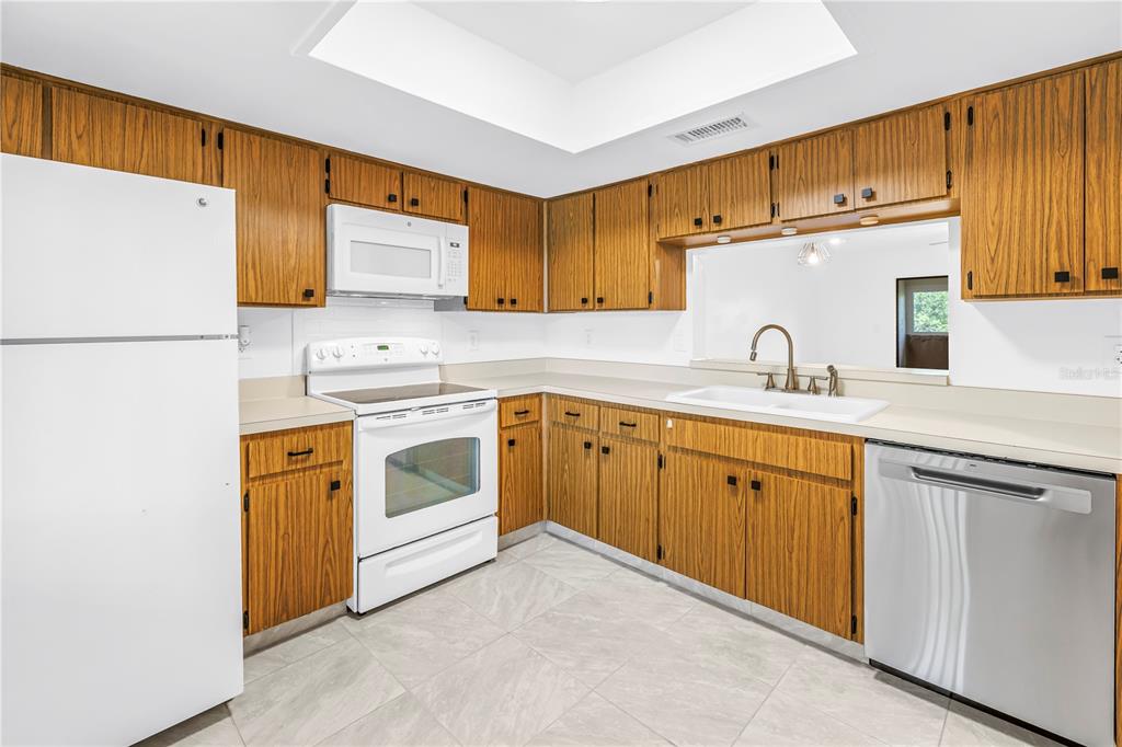 A kitchen features wood cabinets, white appliances, a stainless steel dishwasher, and light tile flooring — 3600 MAGNOLIA RIDGE CIRCLE UNIT 1224, PALM HARBOR, FL