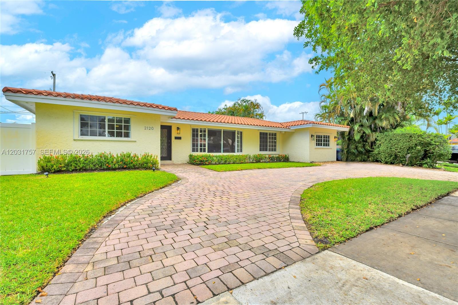 A single-story yellow house features a red tile roof and a paved brick driveway — 2120 NE 207th St, Miami FL 33179, MIAMI, FL