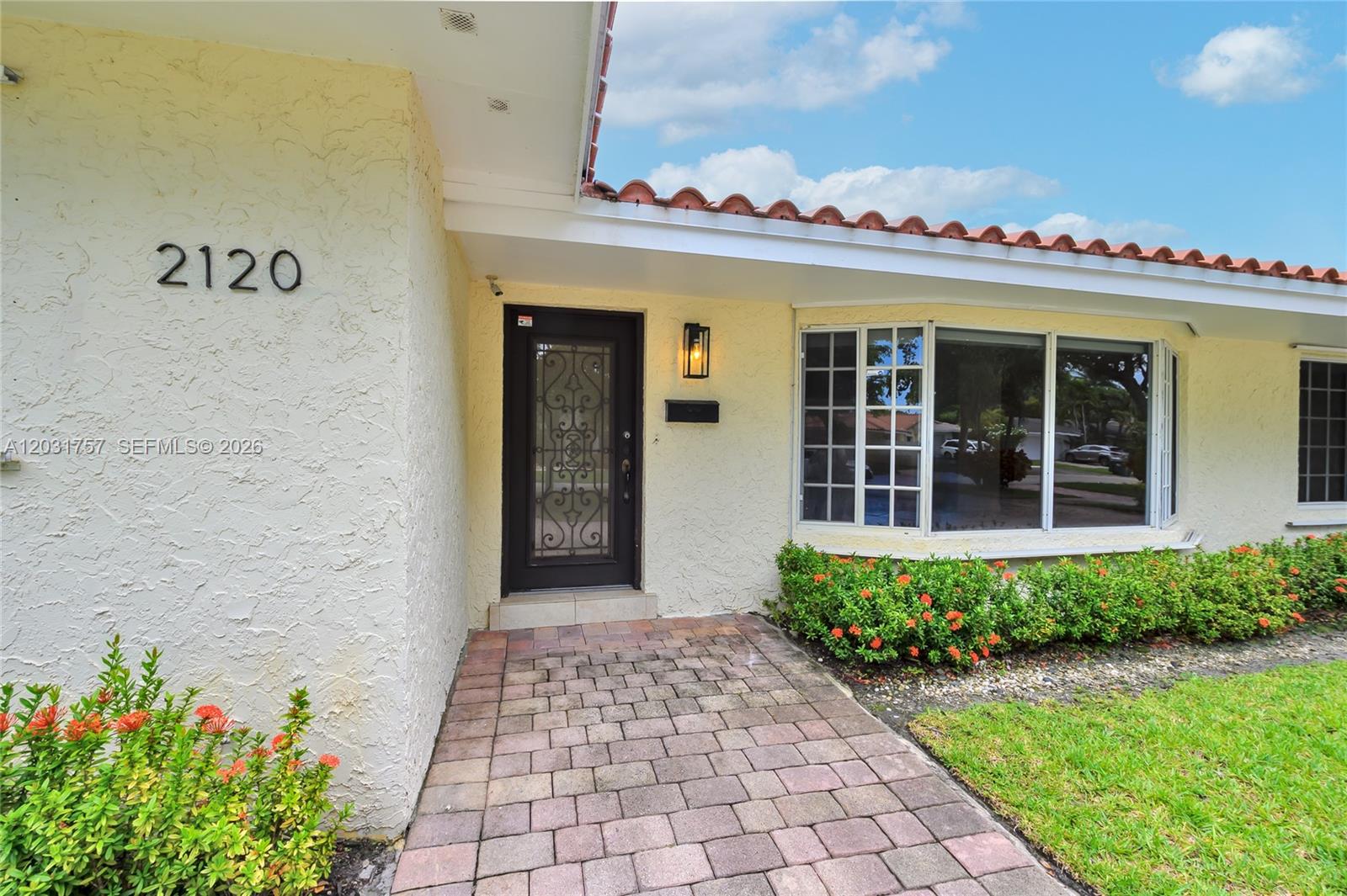 The exterior of a house features a paved walkway, a dark front door, and a bay window — 2120 NE 207th St, Miami FL 33179, MIAMI, FL