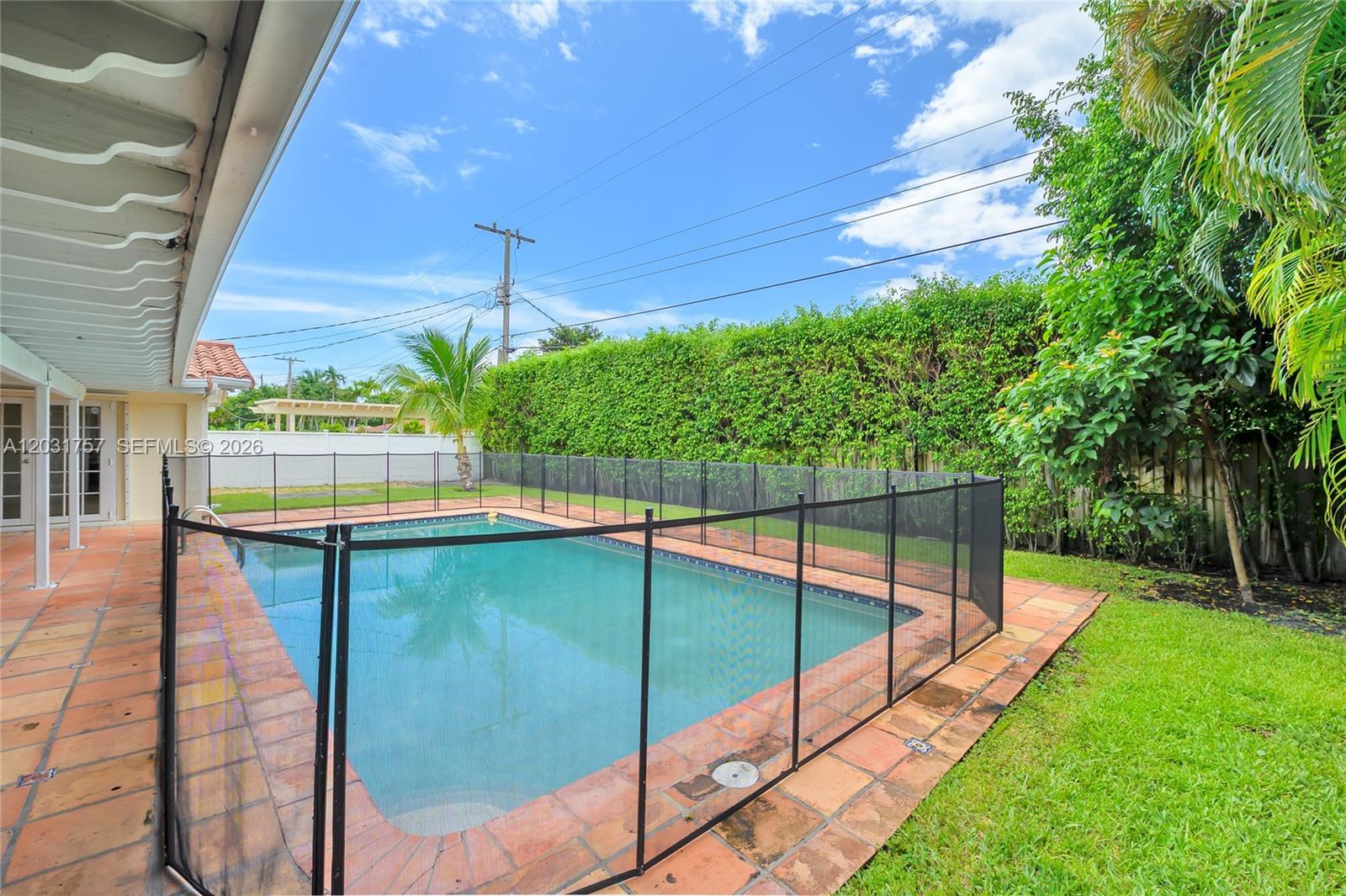 A backyard features a swimming pool enclosed by a black mesh safety fence — 2120 NE 207th St, Miami FL 33179, MIAMI, FL