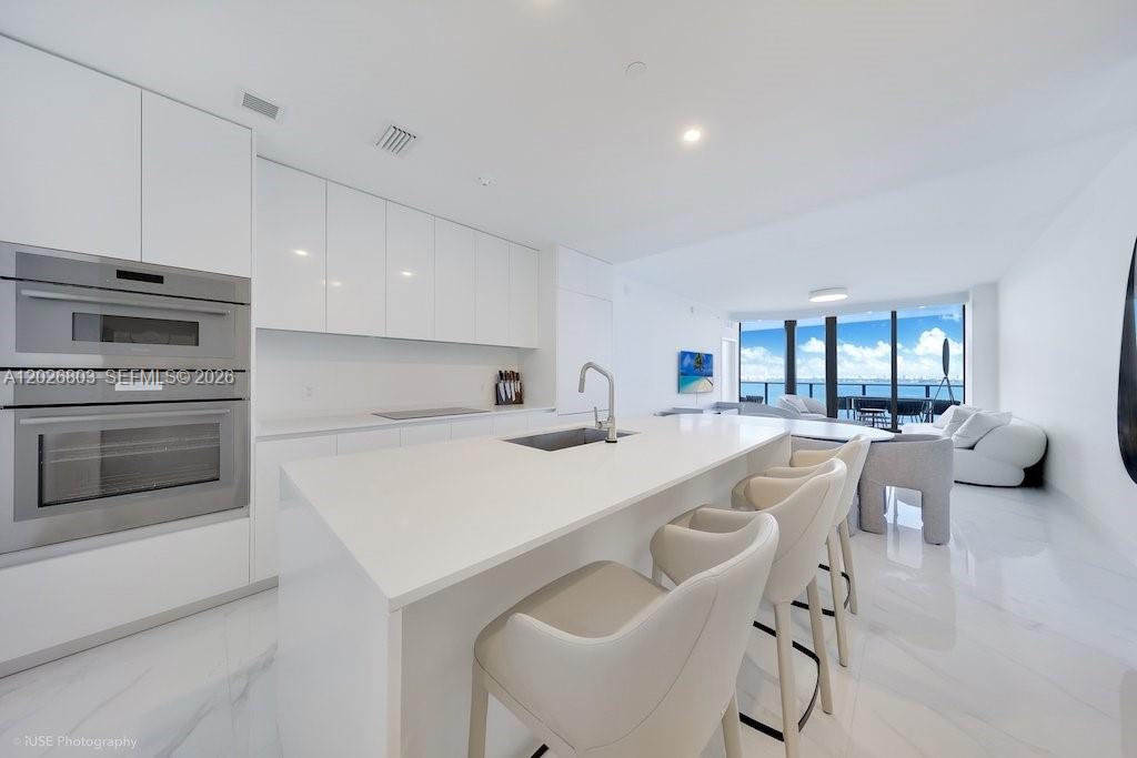 A modern white kitchen features a large island, stainless steel appliances, and floor-to-ceiling windows — 700 NE 24 St # 1403, Miami FL 33137, MIAMI, FL