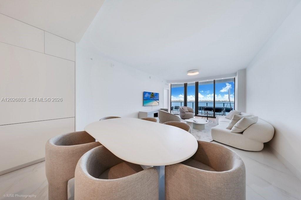 A modern, white-walled living and dining area features a curved sofa and floor-to-ceiling windows — 700 NE 24 St # 1403, Miami FL 33137, MIAMI, FL
