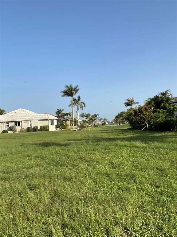 A grassy vacant lot sits next to a residential house with palm trees in the background — 3701 BORDEAUX DRIVE, PUNTA GORDA, FL
