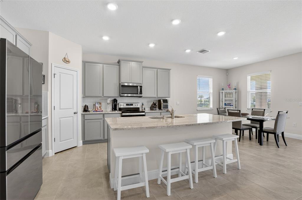 A kitchen features gray cabinets, a stone-topped island with four stools, and a dining area — 152 BRIGHT IBIS AVENUE, APOLLO BEACH, FL