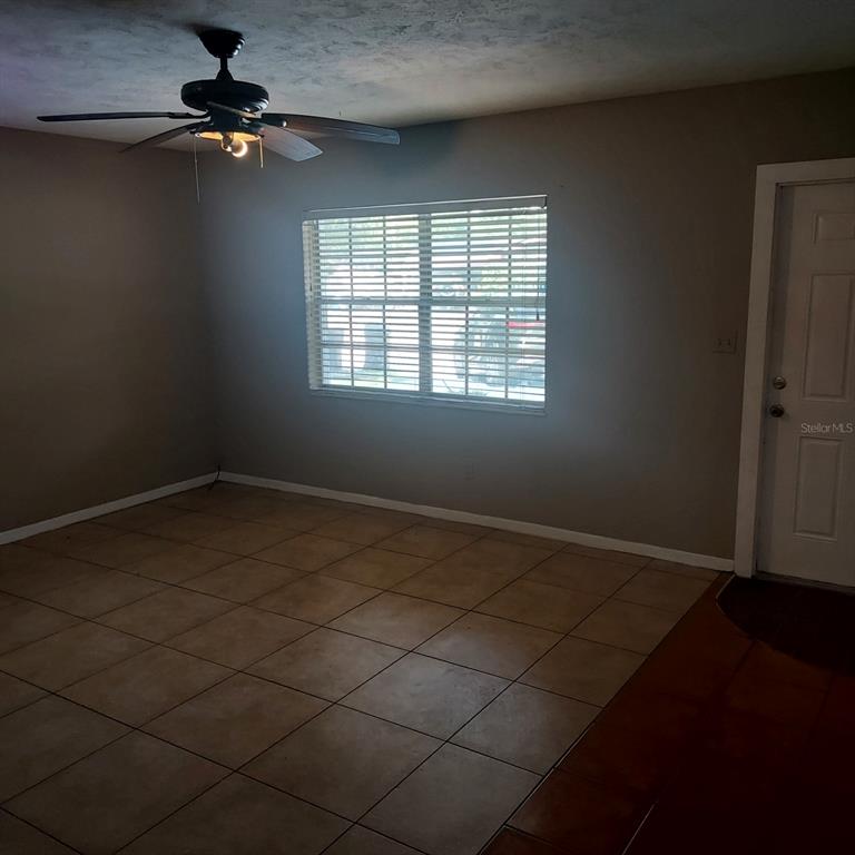An empty room features tan tile flooring, a ceiling fan, and a window with blinds — 4617 SNOOK DRIVE, TAMPA, FL