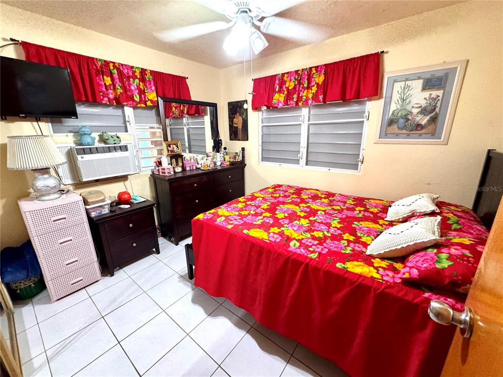 A bedroom features a bed with a floral red spread, tile flooring, and window valances — Carretera #970 BO. MAIZALES, NAGUABO, PR