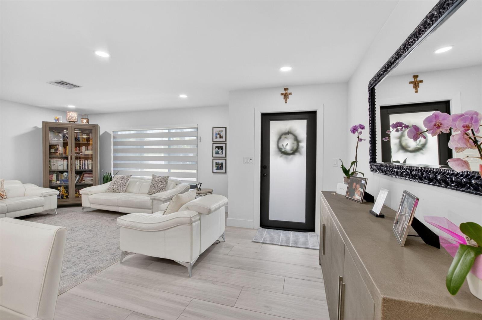 A bright living room features white leather sofas, light wood-look flooring, and a black-framed door — 658 NW 7th Avenue, Boca Raton FL 33486, BOCA RATON, FL