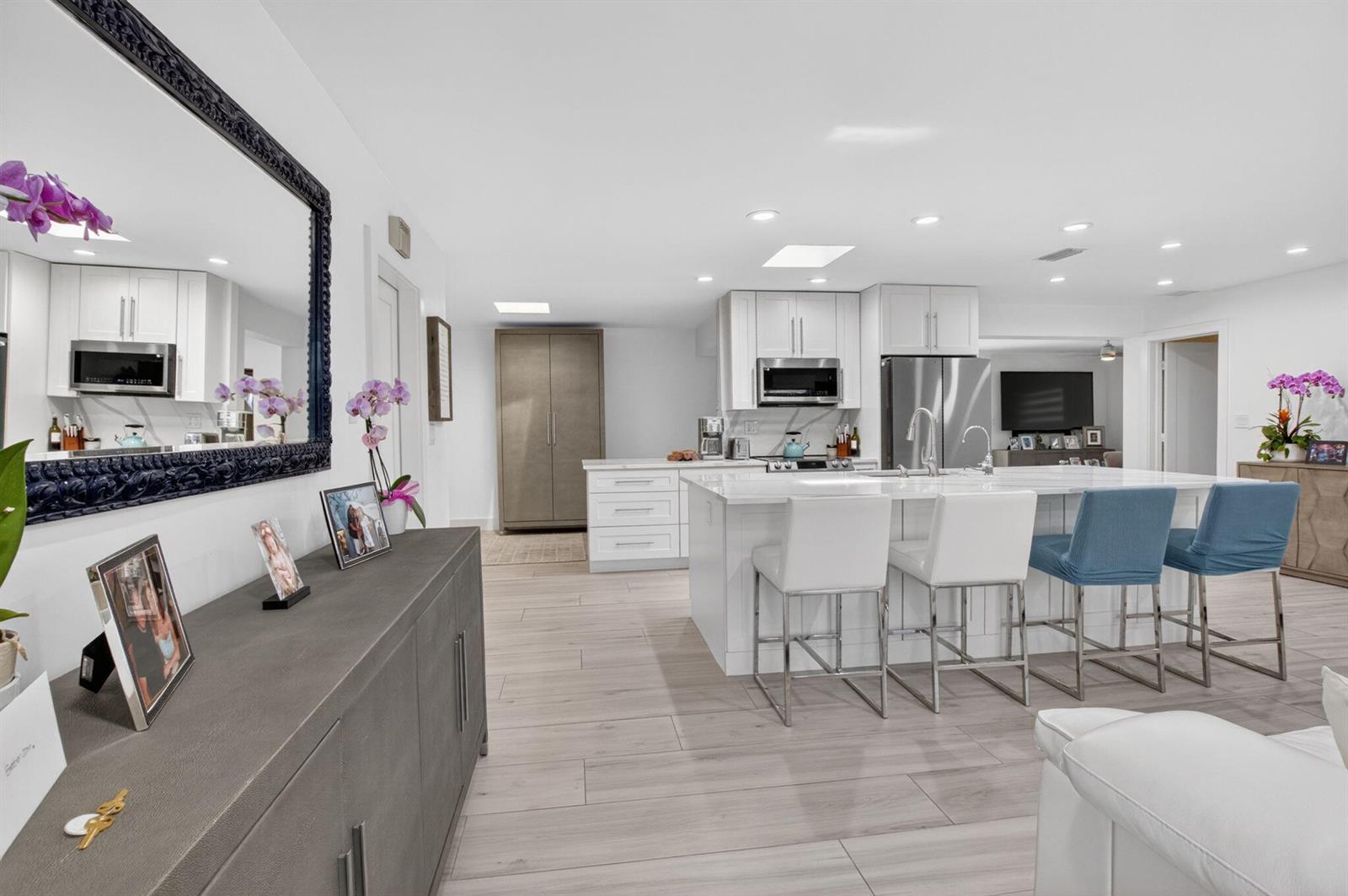 A modern kitchen features white cabinetry, a large island with bar seating, and light flooring — 658 NW 7th Avenue, Boca Raton FL 33486, BOCA RATON, FL