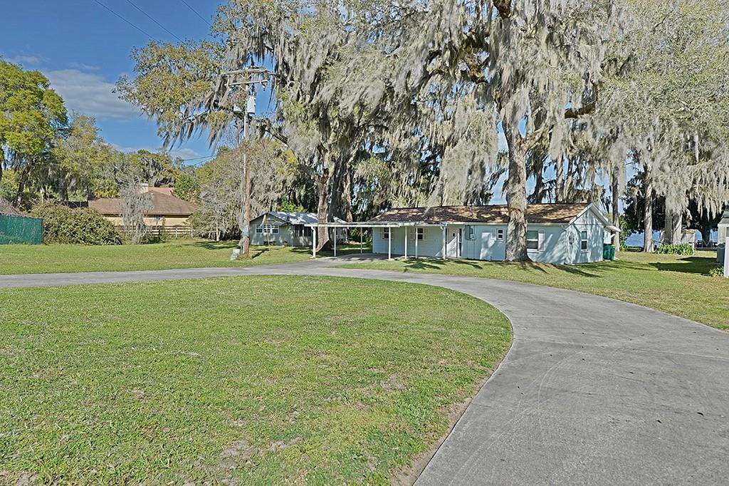 A light blue house with a carport sits on a grassy lot with large trees — 426 ELLA AVENUE, INVERNESS, FL