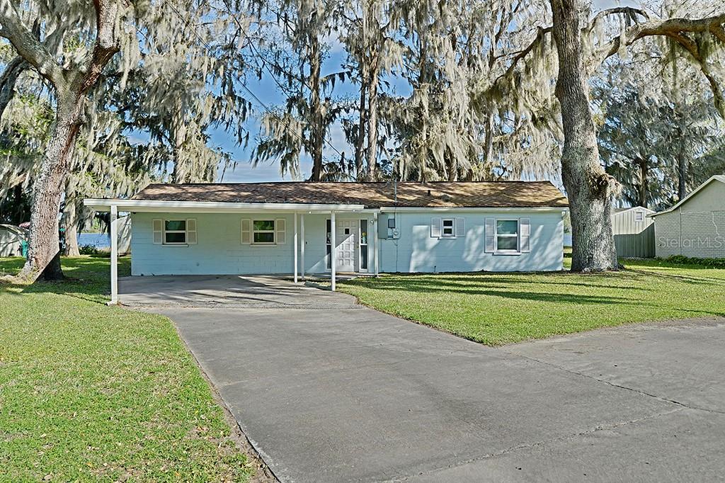 A single-story house with a carport and light blue siding sits under large oak trees — 426 ELLA AVENUE, INVERNESS, FL