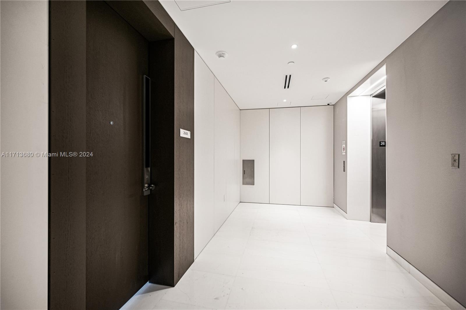 A modern apartment hallway features a dark wood door, white walls, and an elevator entrance — 300 Biscayne Blvd Way # 2608, Miami FL 33131, MIAMI, FL