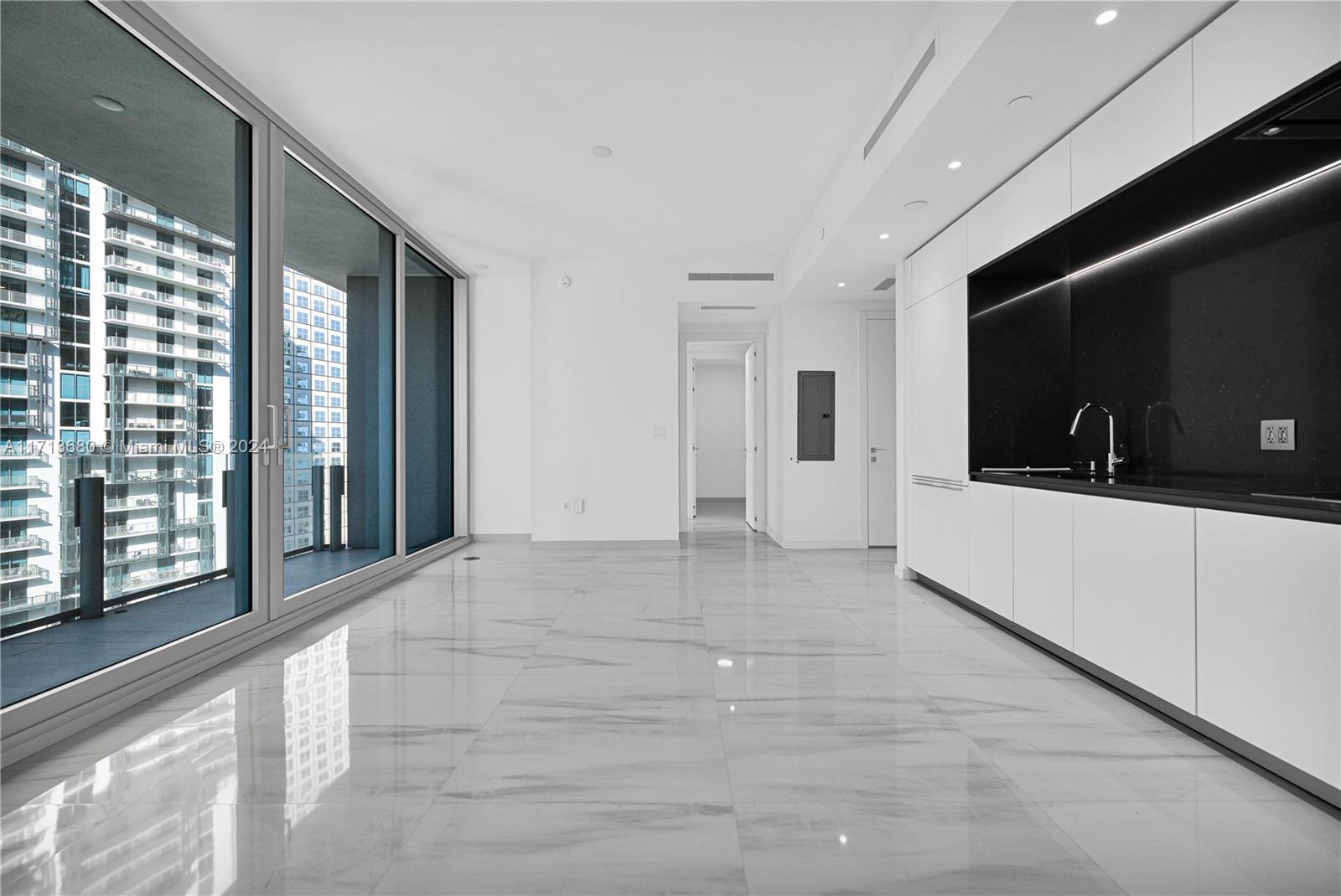 A modern kitchen with white cabinets and black countertops opens into a bright living area — 300 Biscayne Blvd Way # 2608, Miami FL 33131, MIAMI, FL