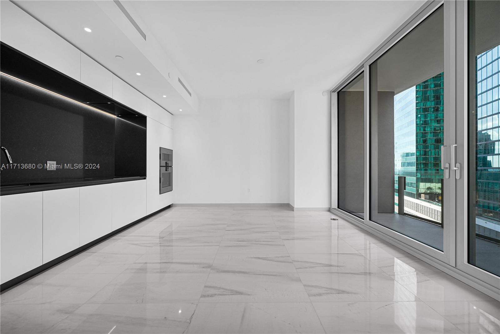 A modern kitchen features white cabinetry, black countertops, and large windows overlooking city buildings — 300 Biscayne Blvd Way # 2608, Miami FL 33131, MIAMI, FL