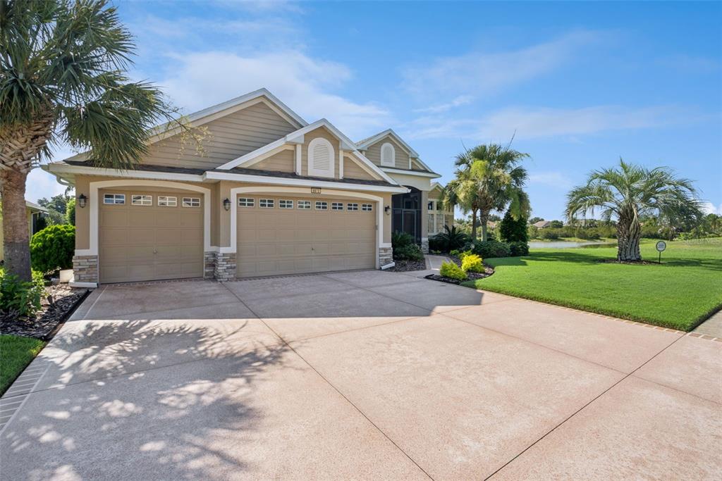 A tan house with a three-car garage and a large driveway sits near a pond — 8872 BRIDGEPORT BAY CIRCLE, MOUNT DORA, FL