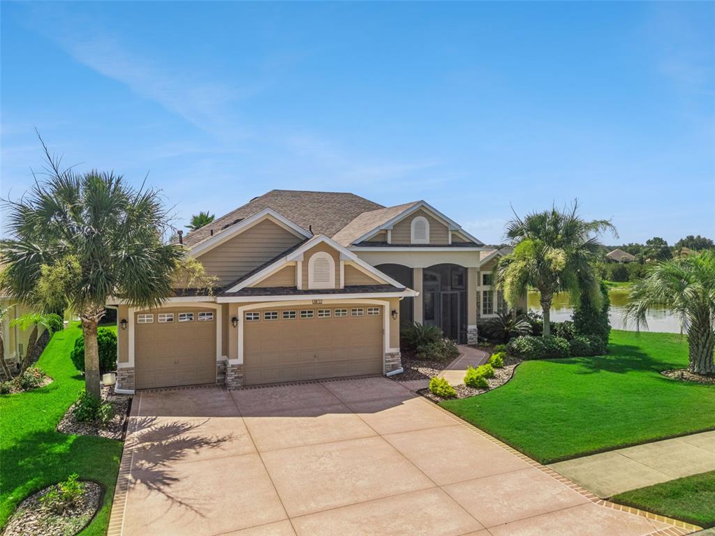 A single-story suburban house with a three-car garage, tan siding, and a paved driveway — 8872 BRIDGEPORT BAY CIRCLE, MOUNT DORA, FL