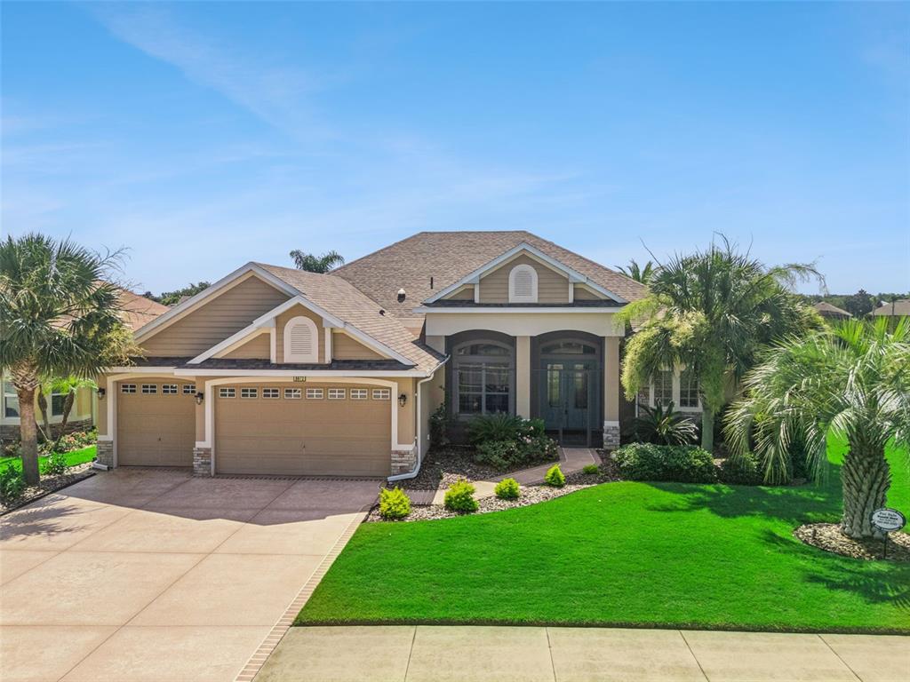A single-story suburban house with a tan exterior, three-car garage, and a manicured front lawn — 8872 BRIDGEPORT BAY CIRCLE, MOUNT DORA, FL