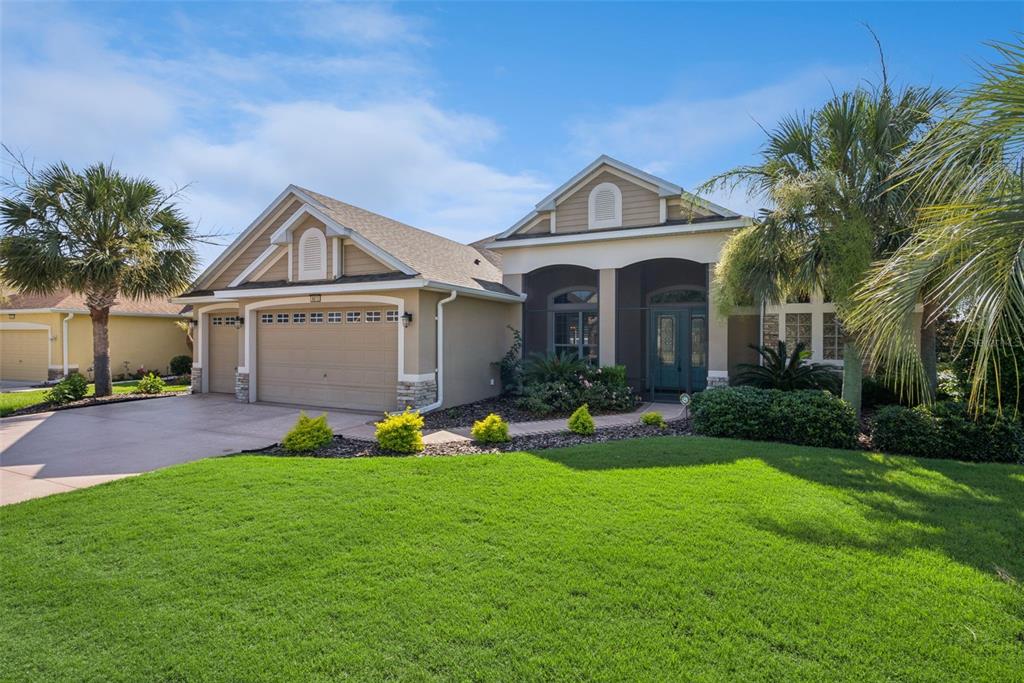 A tan single-story house with a two-car garage, arched entryway, and a manicured front lawn — 8872 BRIDGEPORT BAY CIRCLE, MOUNT DORA, FL