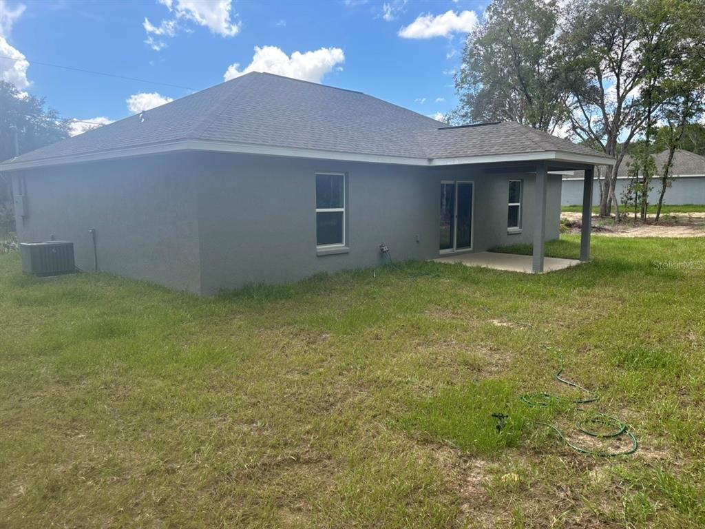 The rear exterior of a gray stucco house features a covered patio and sliding doors — 651 W BANCROFT DRIVE, DUNNELLON, FL
