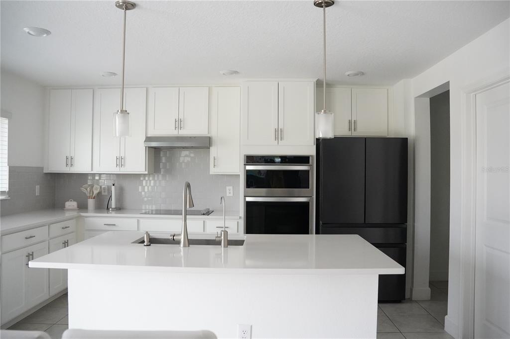 A modern kitchen features white cabinetry, a white quartz island, and black stainless steel appliances — 16436 WINDING PRESERVE CIRCLE, CLERMONT, FL