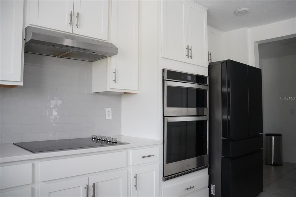 A kitchen features white cabinets, stainless steel appliances, a black refrigerator, and a subway tile backsplash — 16436 WINDING PRESERVE CIRCLE, CLERMONT, FL