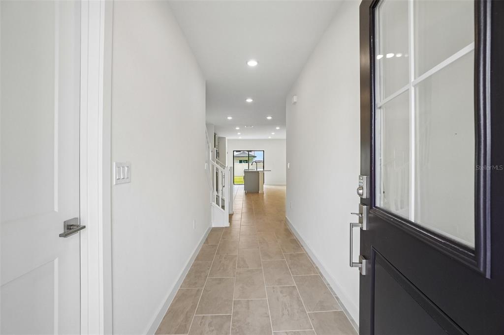 A view from an entryway looking down a tiled hallway toward a kitchen and window — 3237 CUP DRIVE, LAKELAND, FL