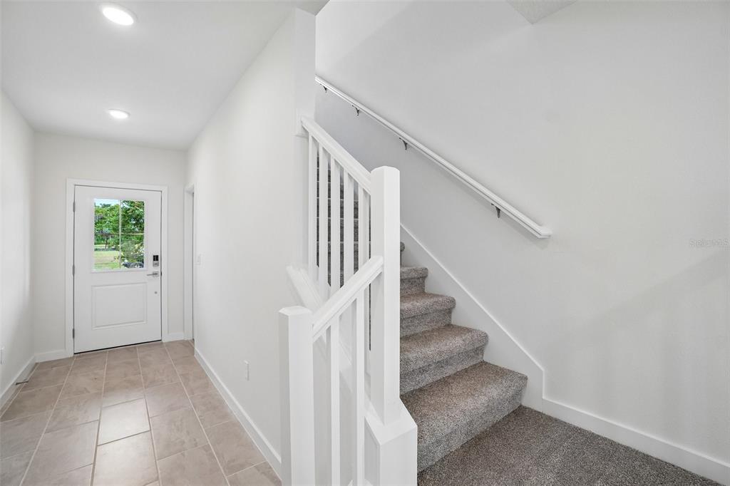 A bright entryway features tiled flooring, a white front door, and carpeted stairs with railings — 3237 CUP DRIVE, LAKELAND, FL