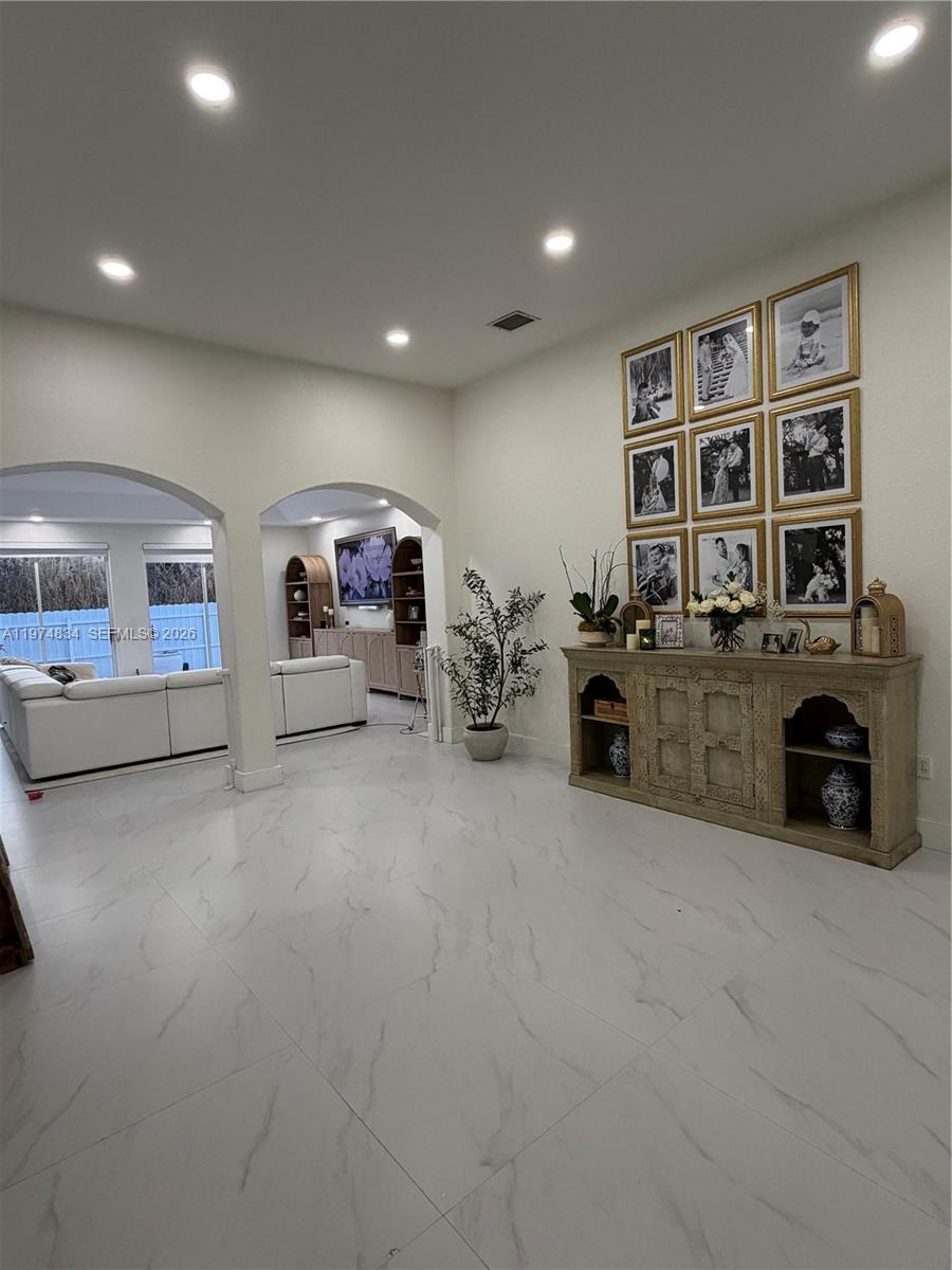 A bright living area features white tile floors, arched entryways, and a gallery wall display — 3744 SW 156th Ct, Miami FL 33185, MIAMI, FL