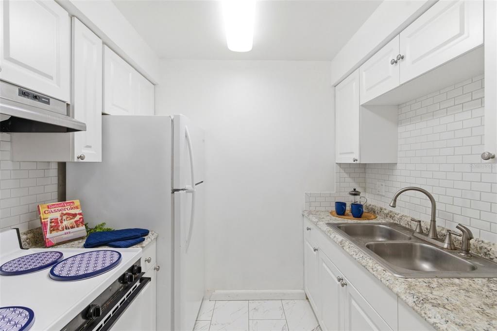 A galley kitchen features white cabinets, granite countertops, a subway tile backsplash, and white appliances — 2353 SHELLEY STREET UNIT 19, CLEARWATER, FL