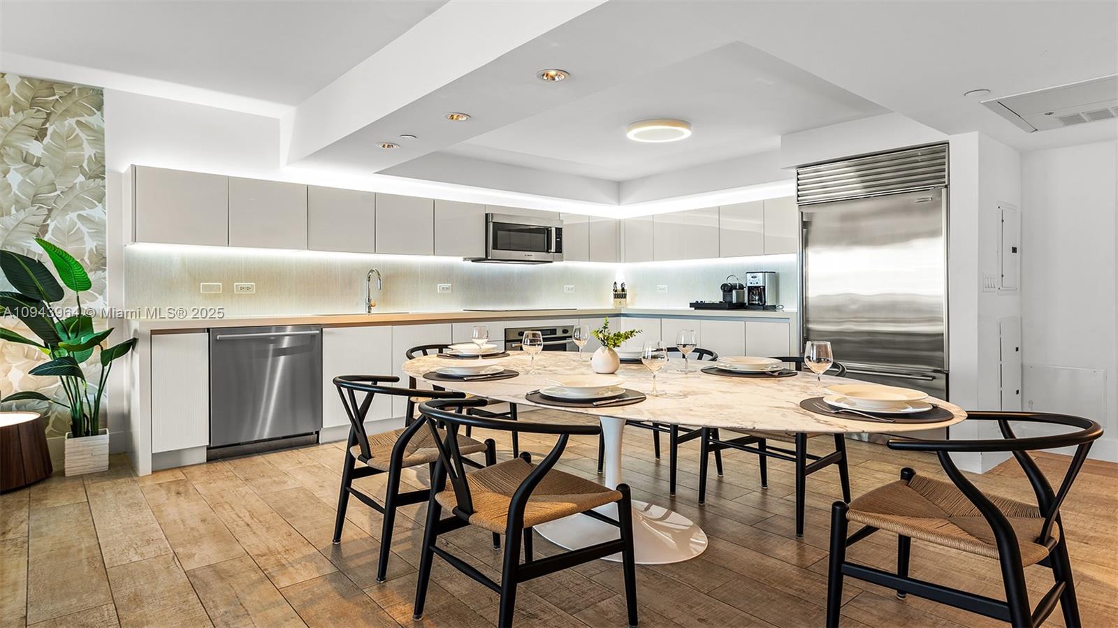 A modern kitchen features white cabinetry, stainless steel appliances, and an oval dining table — 102 24th St # 1120, Miami Beach FL 33139, MIAMI BEACH, FL