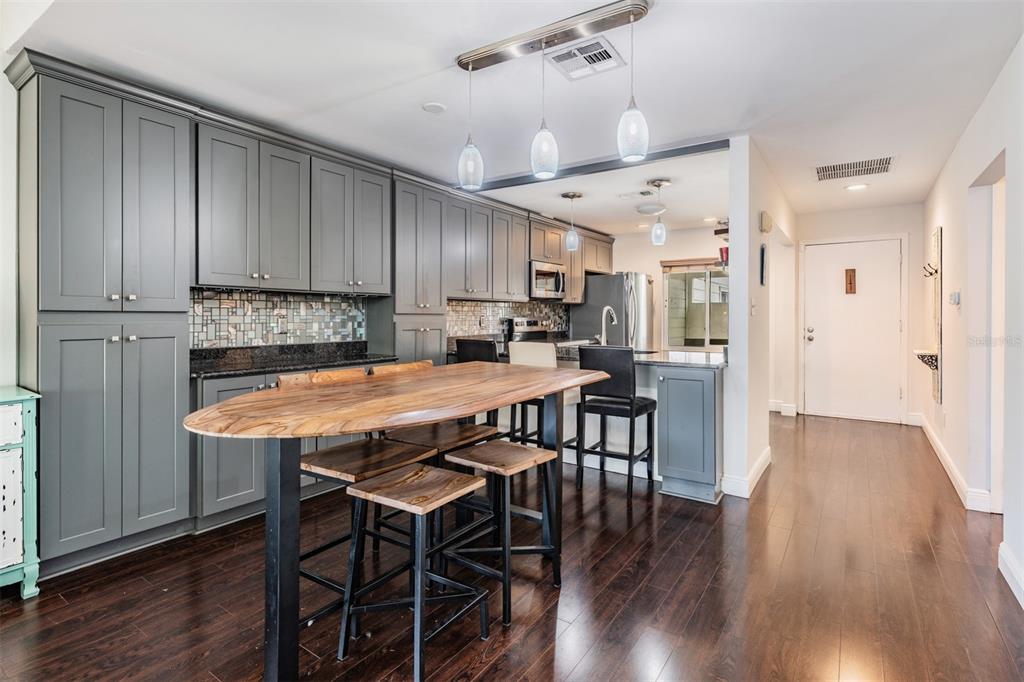 A kitchen features gray cabinetry, a wooden island with bar stools, and dark hardwood floors — 637 DRAKE LANE N, DUNEDIN, FL
