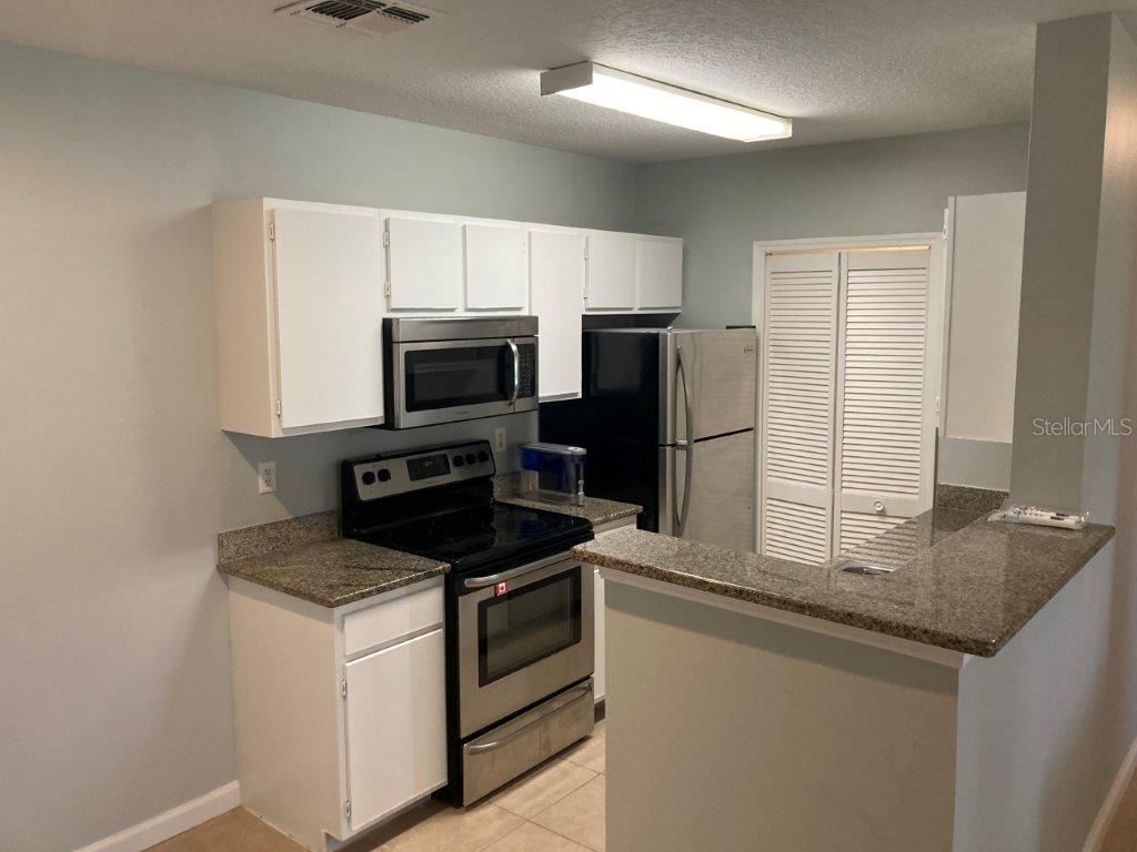 A kitchen features white cabinets, stainless steel appliances, and granite countertops — 4352 S KIRKMAN ROAD UNIT 1211, ORLANDO, FL